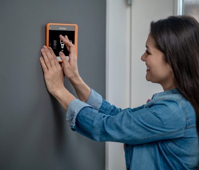 Life style. Happy woman with long dark hair touching smart home device monitor hanging on wall with hands choosing mode in daylight